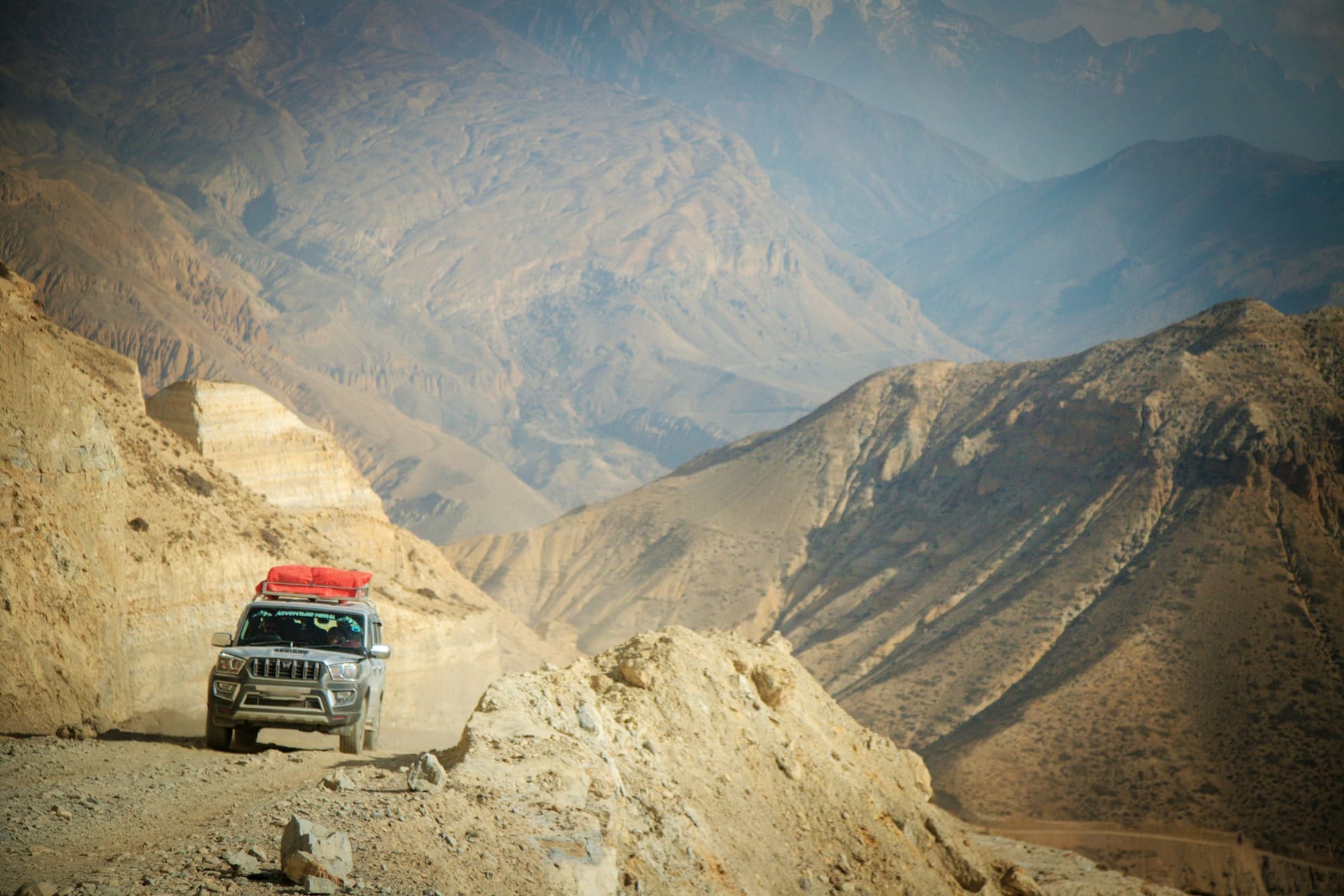 A Mahindra Scorpio with luggage on its roof, driving a dusty mountain road in Upper Mustang, Nepal