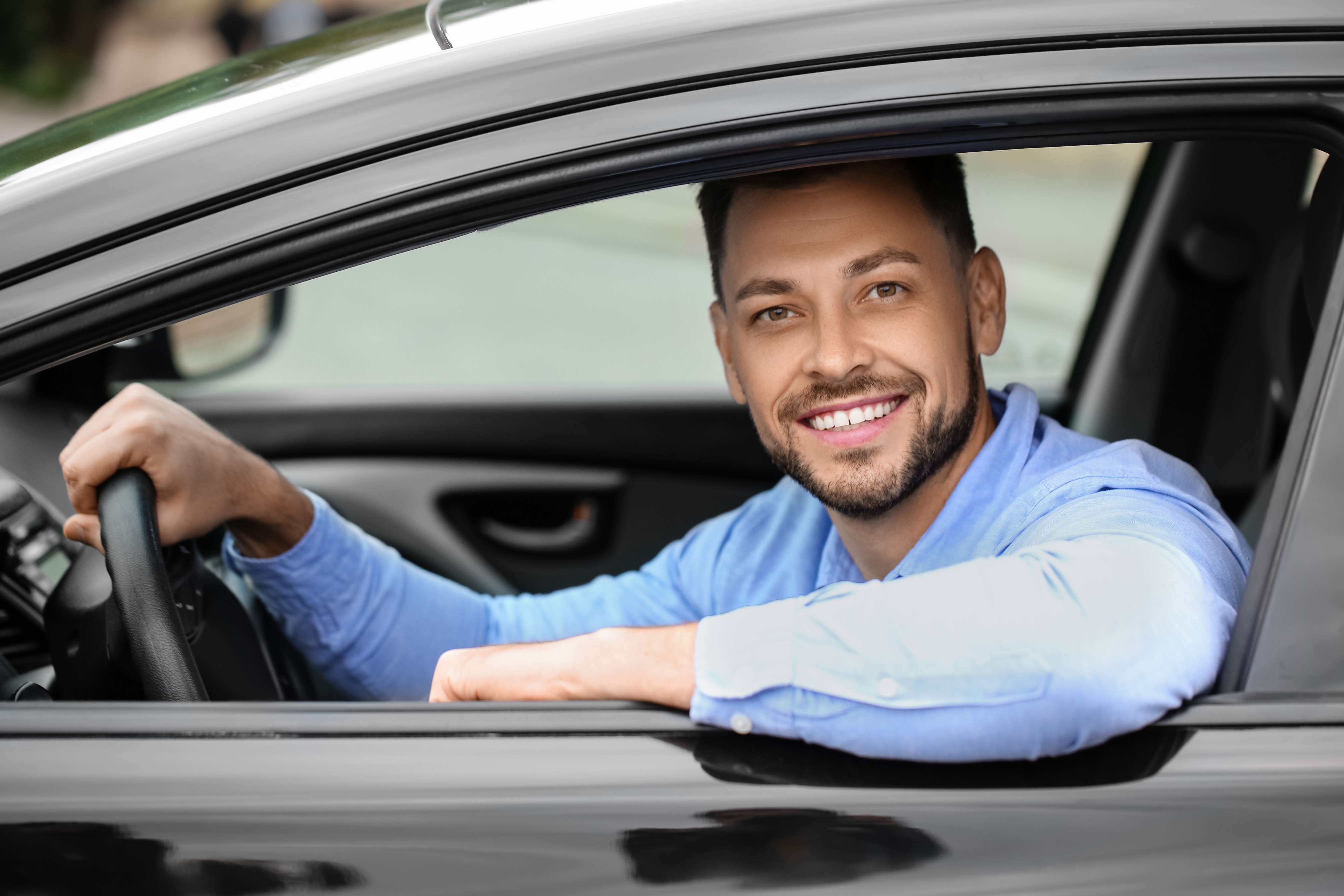 A smiling driver at the wheel, leaning on the open car window