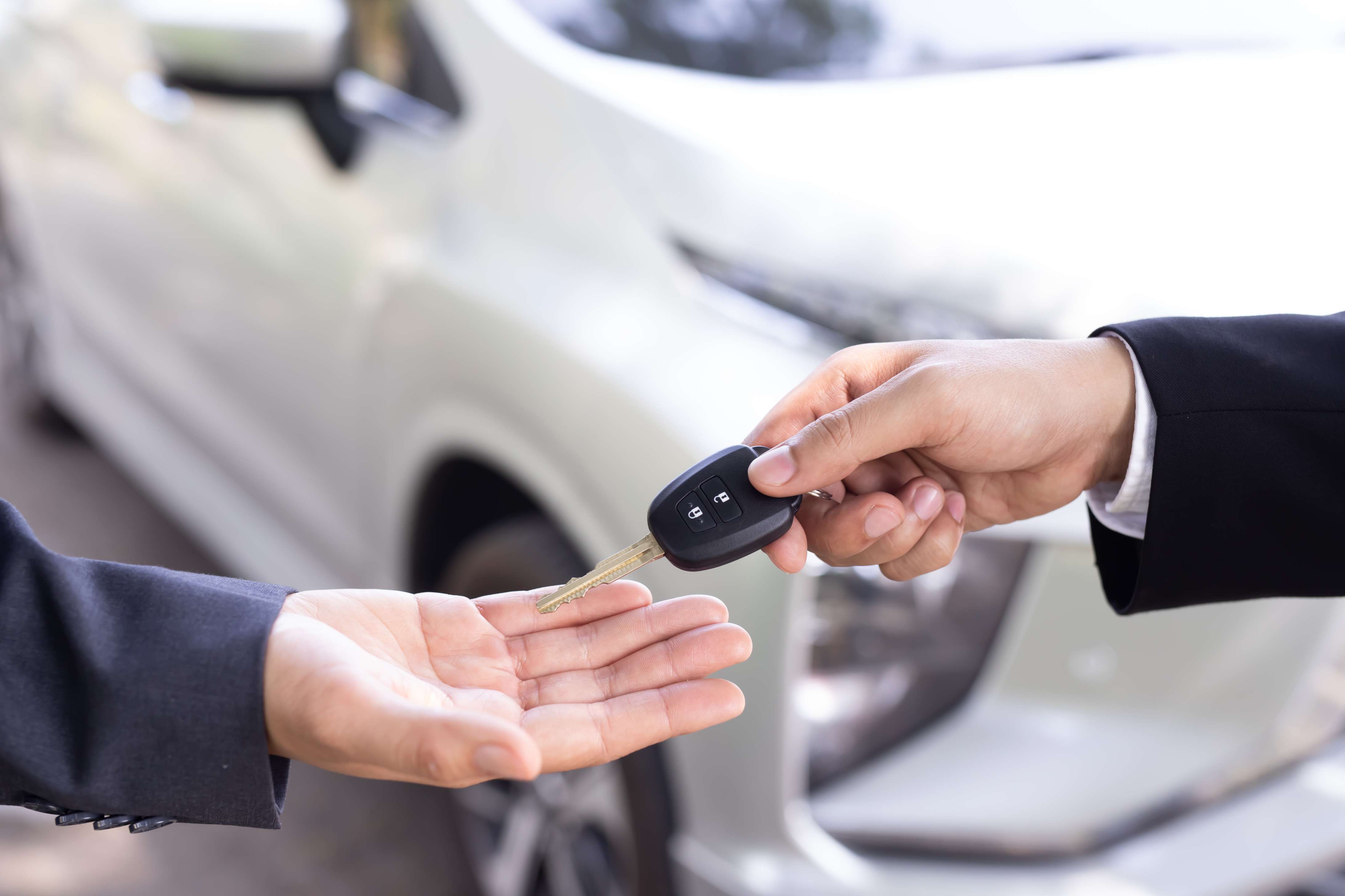 Car keys handed from owner to renter beside a silver car